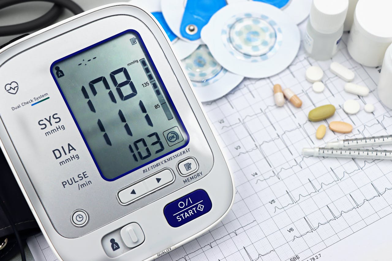 Home Close-up of a digital blood pressure monitor with ECG printout, pills, and medical tools.