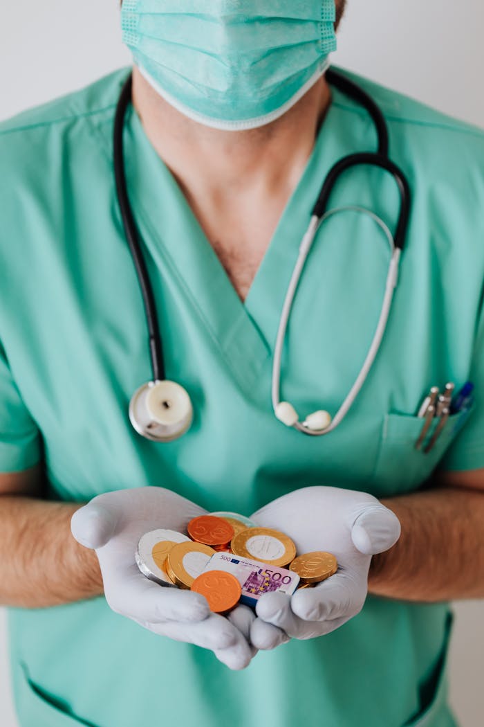 Services Anonymous male doctor wearing medical uniform mask and latex gloves holding coins and plastic euro while standing near white wall in clinic