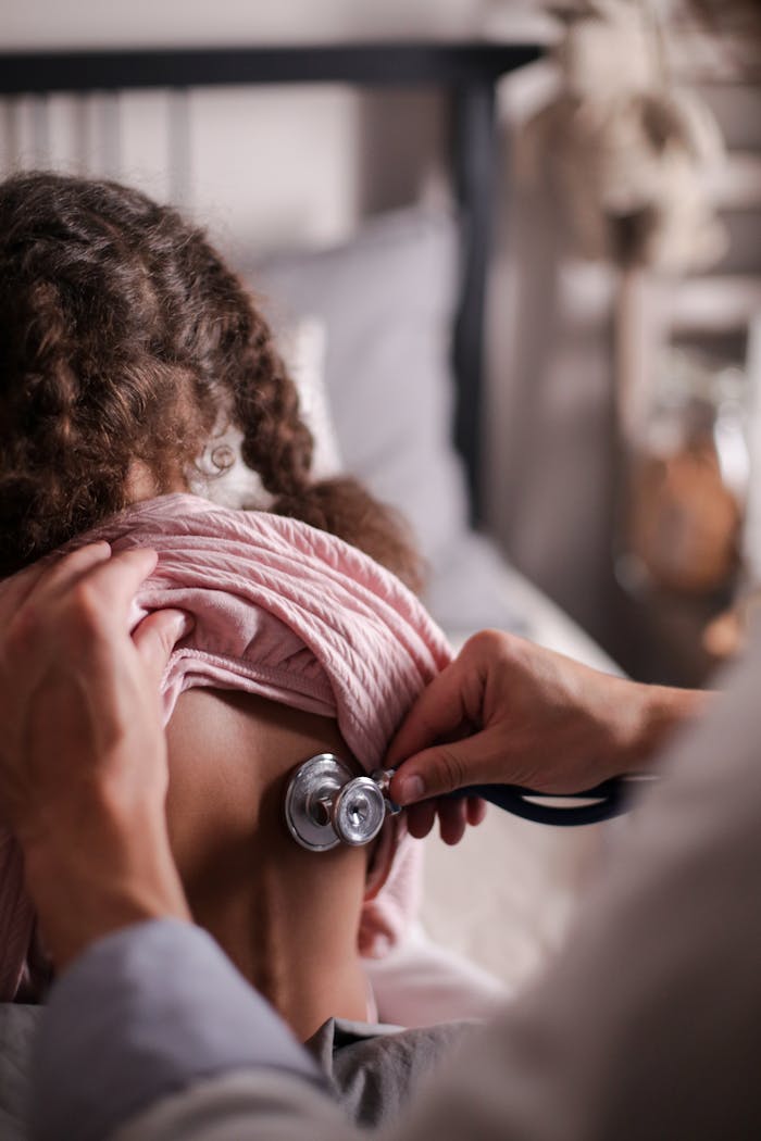 Services Doctor using stethoscope to check child's back during a health examination indoors.